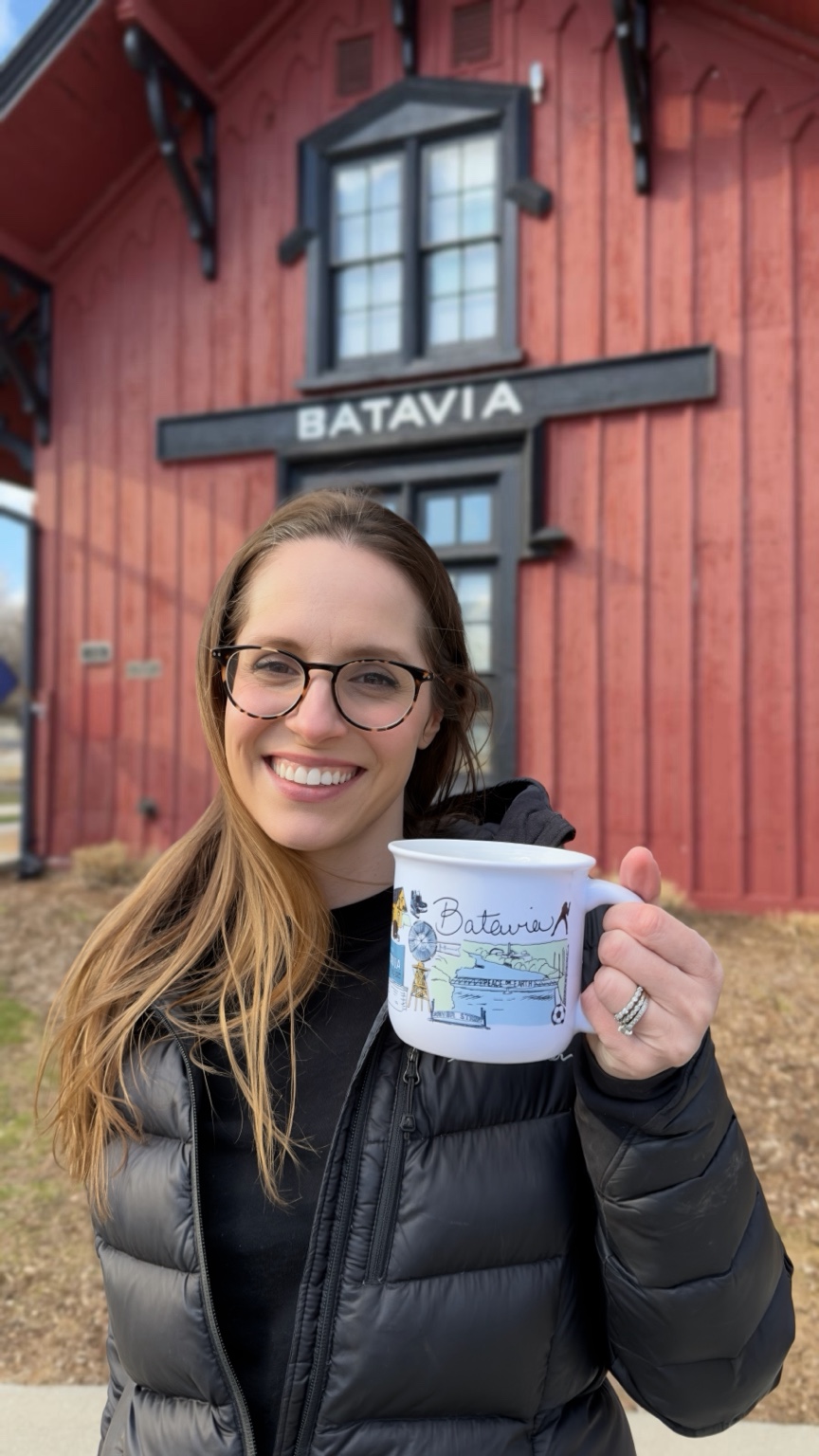 Artist Ashley Ann holding The Batavia Mug in front of the historic Batavia Depot