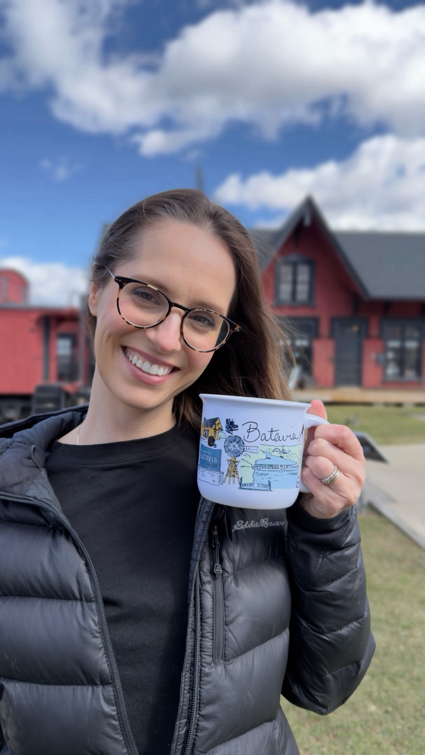 Artist Ashley Ann holding The Batavia Mug along the Batavia riverfront