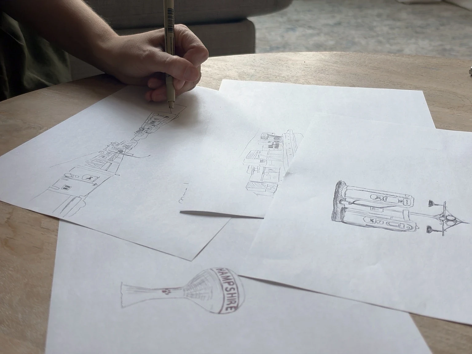 Ashley Ann working in pen on Hampshire storefront drawings beside sketches of the Hampshire water tower and other local buildings
